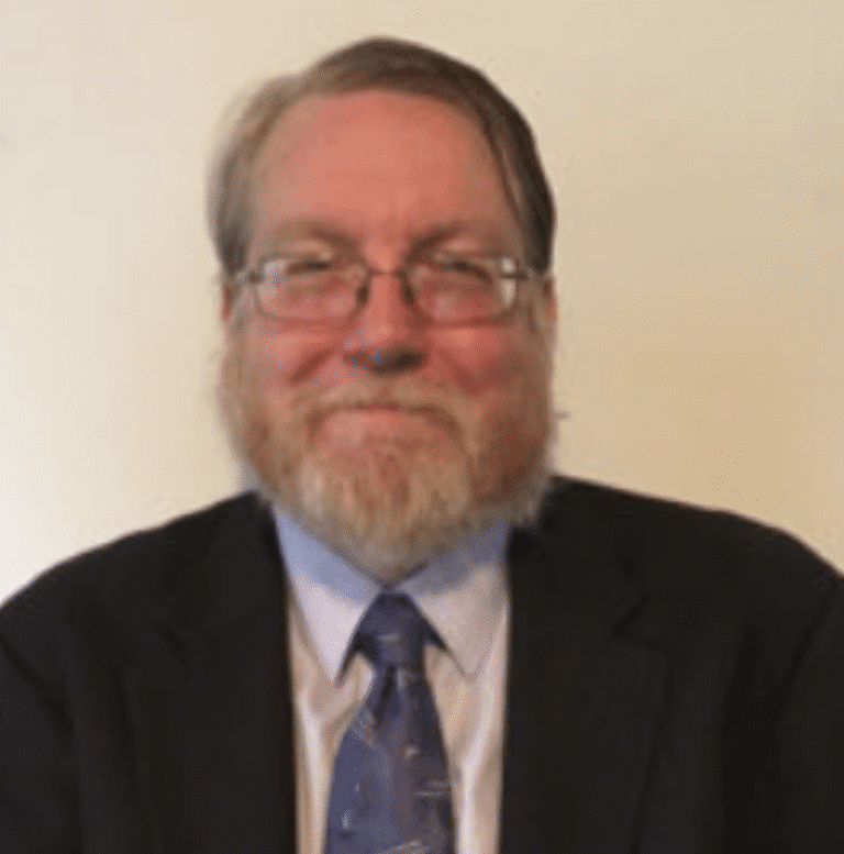 Smiling man with glasses and beard in suit and tie.